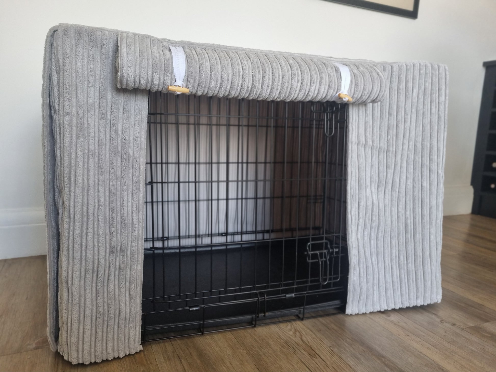 "A black wire dog crate covered with a custom fabric dog crate cover in a grey soft plush design. The aesthetic kennel cover features a minimalist design with a roll-up front panel.