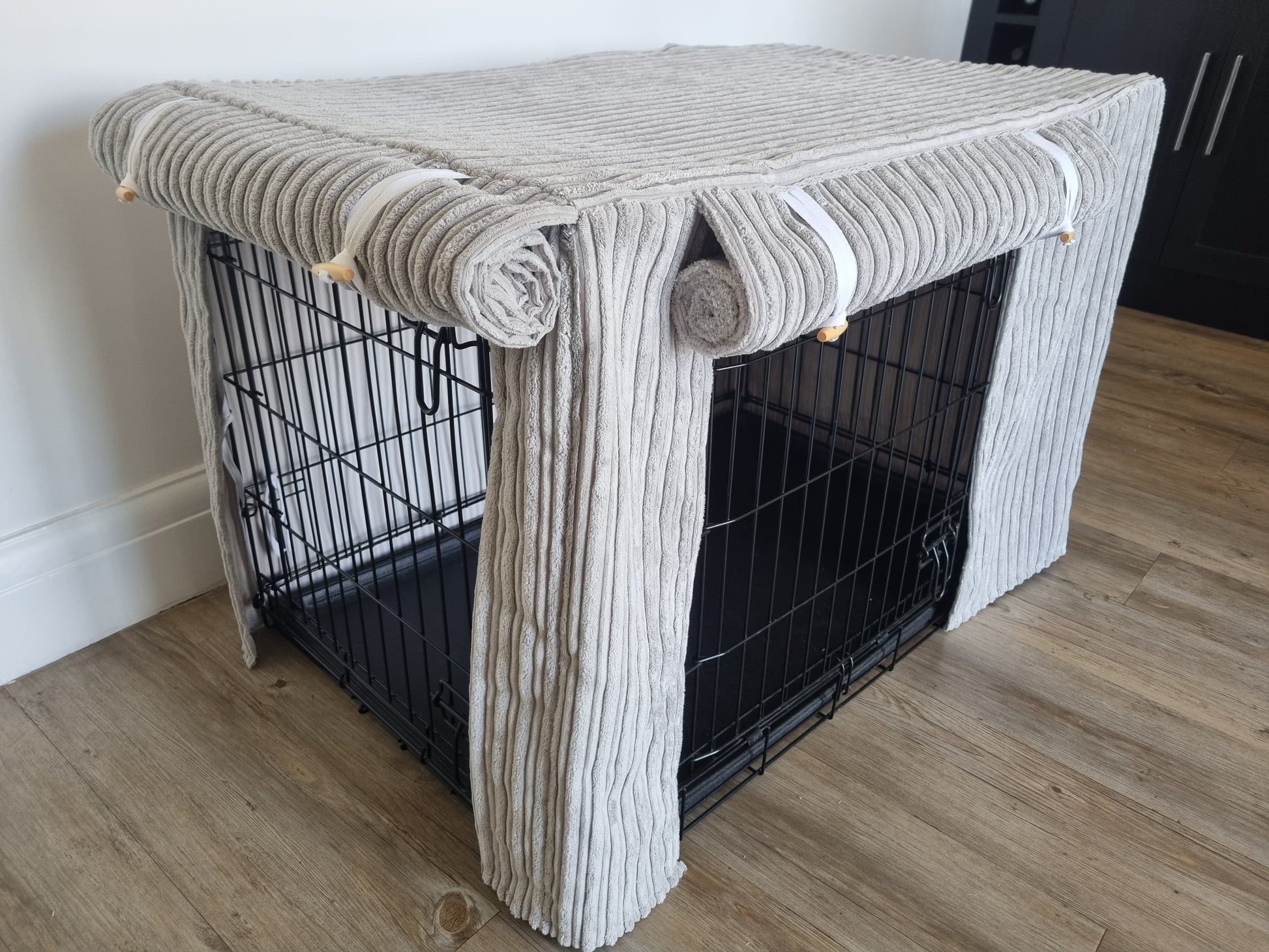 "A black wire dog crate covered with a custom fabric dog crate cover in a grey soft plush design. The aesthetic kennel cover features a minimalist design with a roll-up front panel.