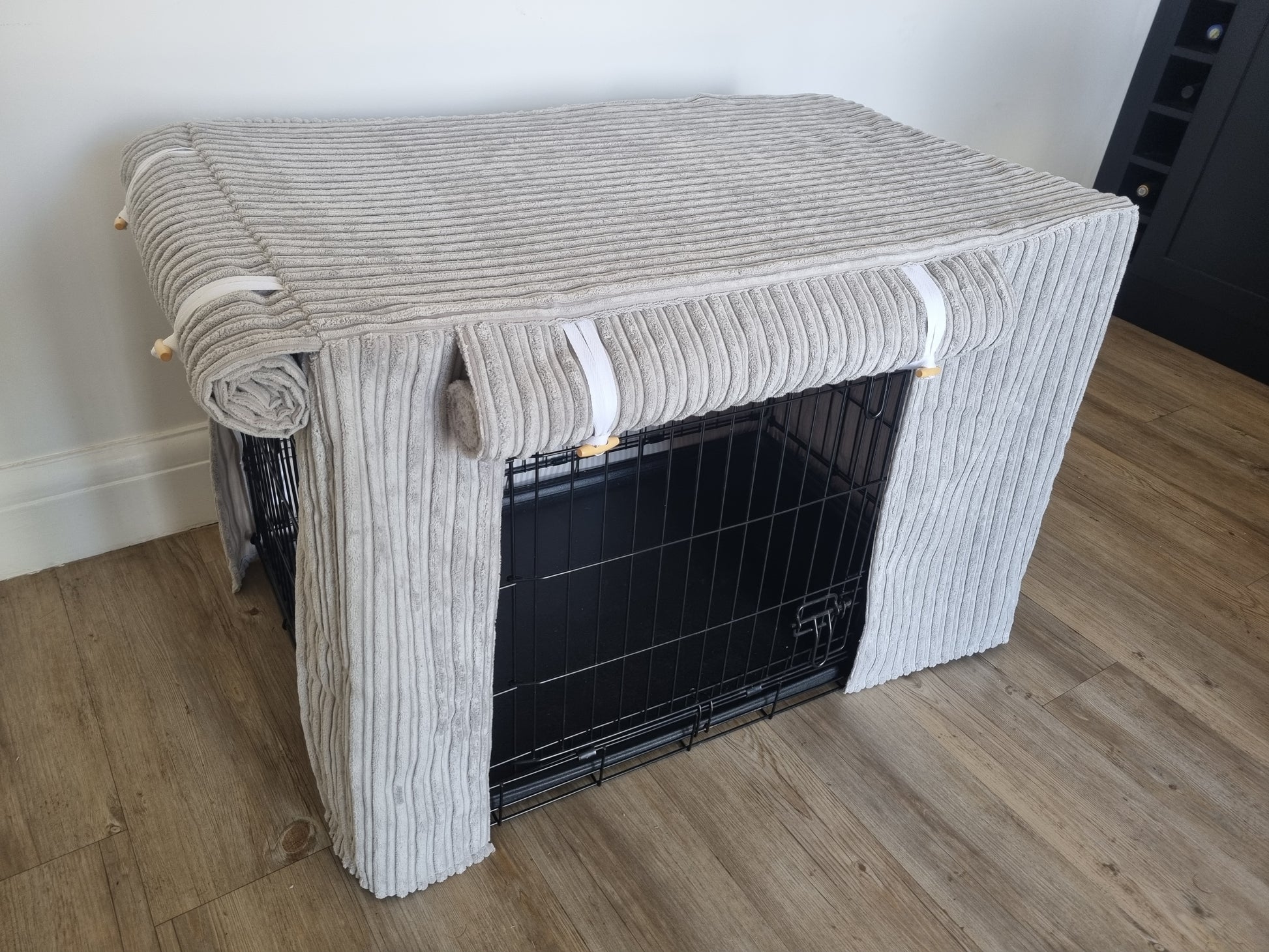 "A black wire dog crate covered with a custom fabric dog crate cover in a grey soft plush design. The aesthetic kennel cover features a minimalist design with a roll-up front panel.